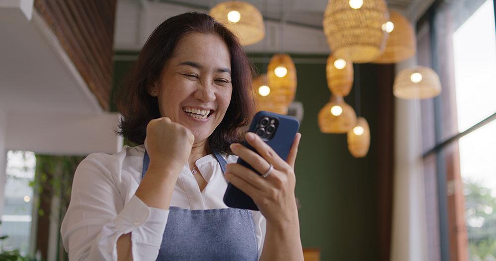 A small business owner looks at her phone and celebrations loan approval