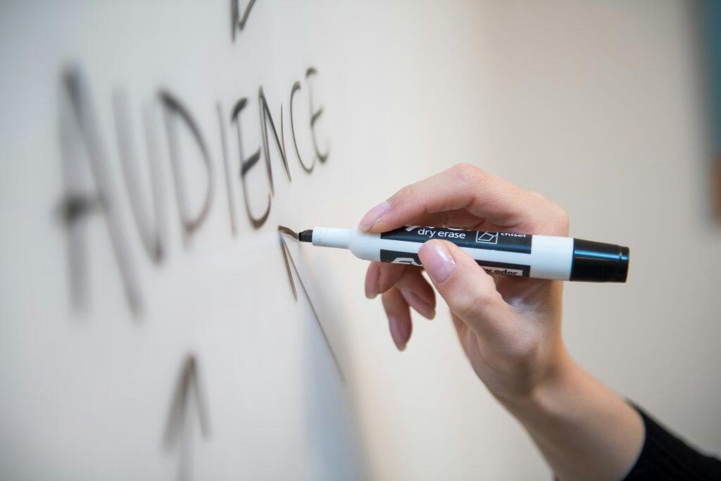 a hand writing on a white board focusing on the audience for social media