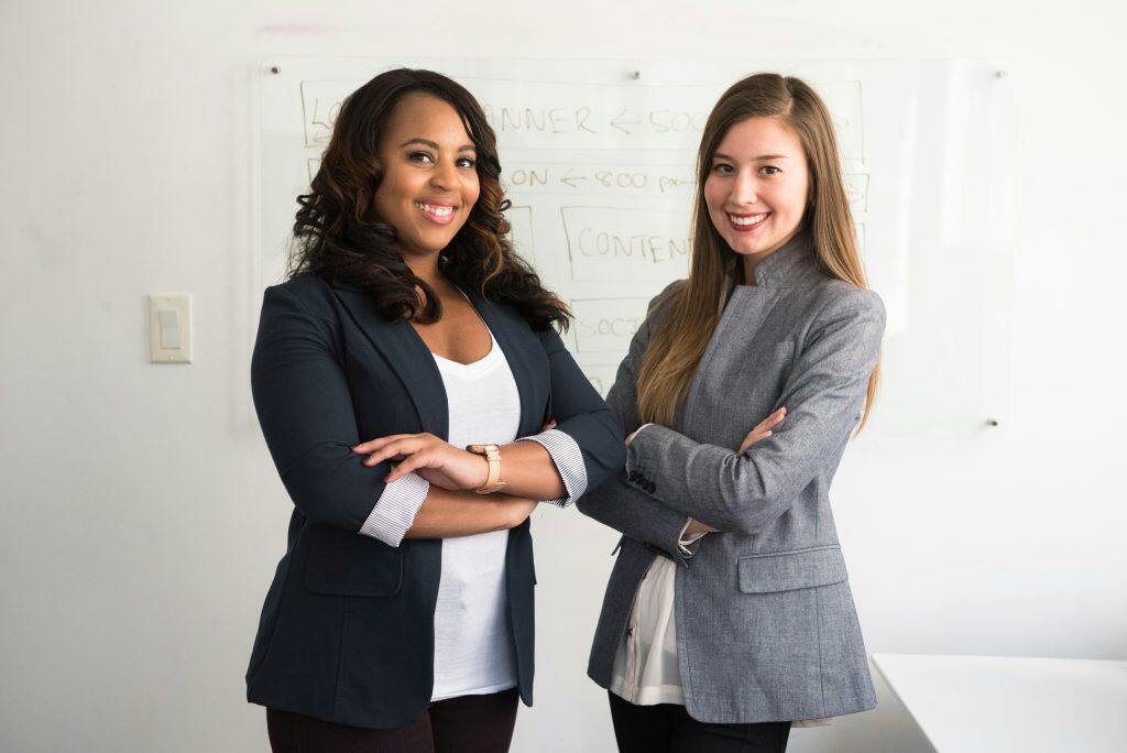 Two professionally dressed individuals, including a Chief Commercial Officer, standing confidently in front of a whiteboard with partially legible notes, suggesting a business or office environment.