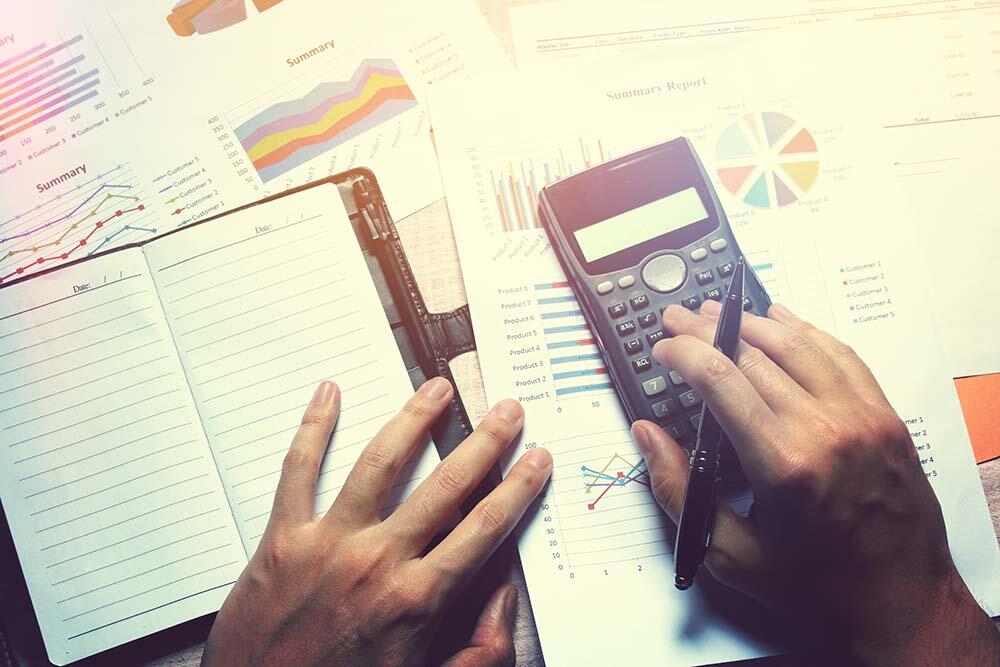 Overhead view of calculator and cluttered graphs on a desk as a worker calculates overhead costs