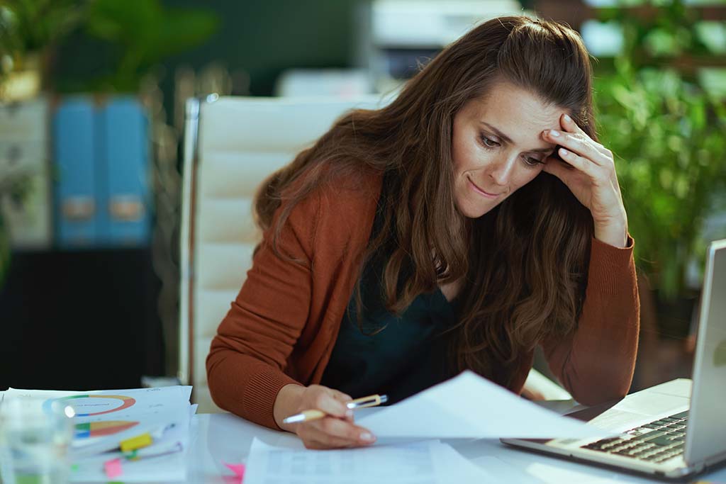 A stressed small business owner holds her head as she examines invoices