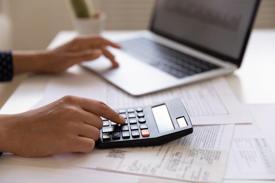 A small business owner completes accounting tasks on a laptop and calculator