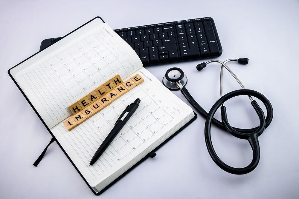 Top view of a notebook with health insurance written on it with small wooden blocks