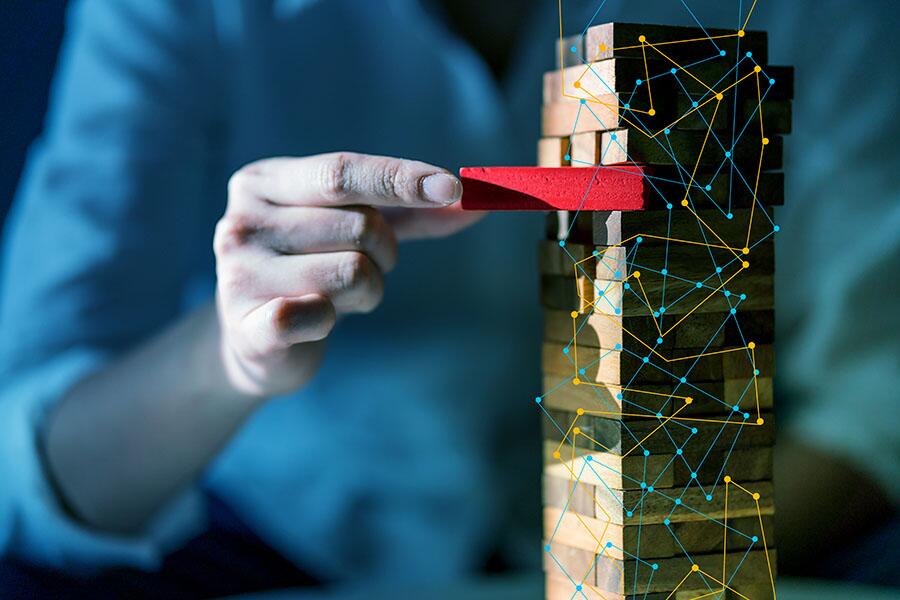 A hand removes a critical block from a wooden stack, representing business strategy and risk management