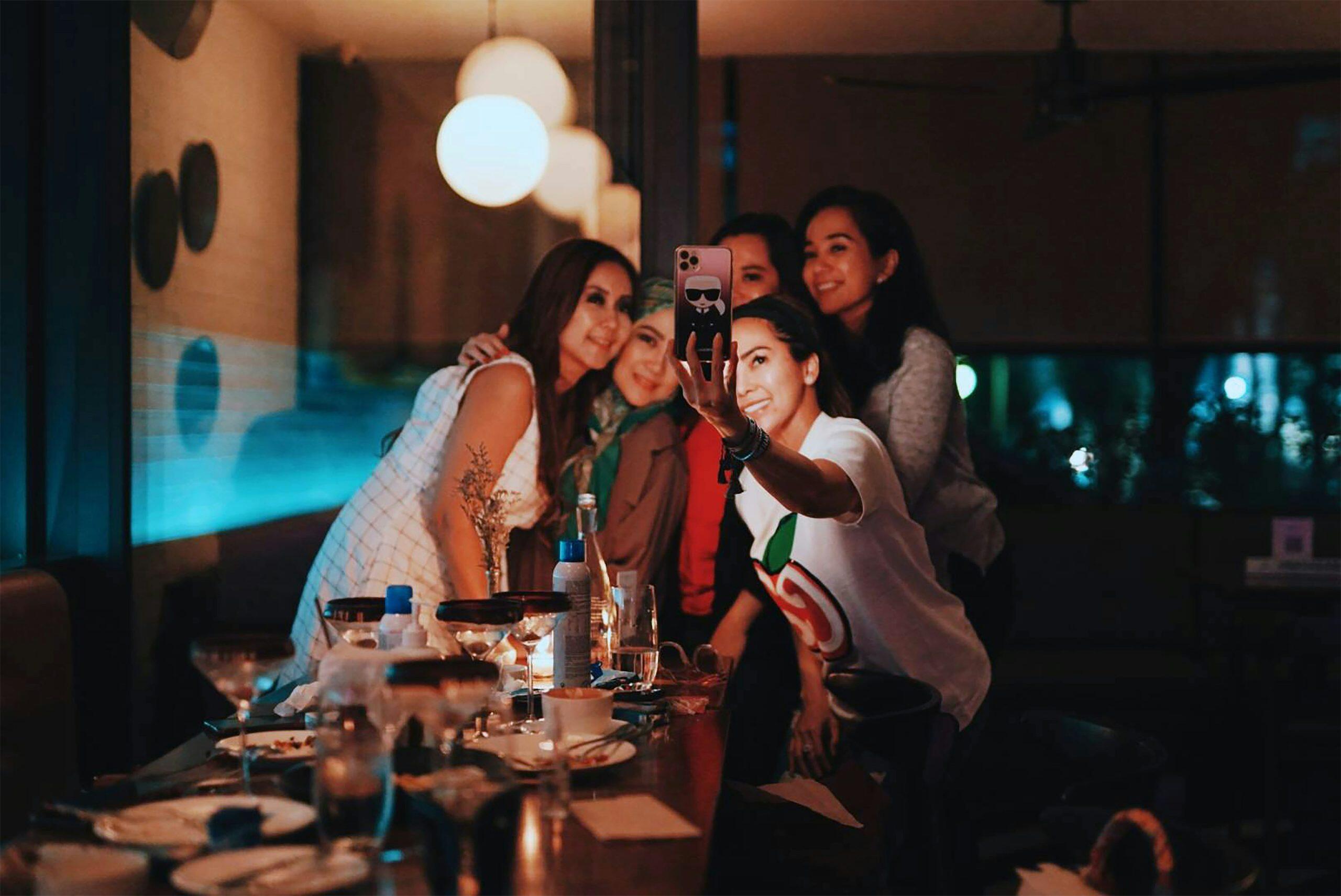 Group of friends taking a selfie at a dining table, symbolizing privacy concerns with employers and social media