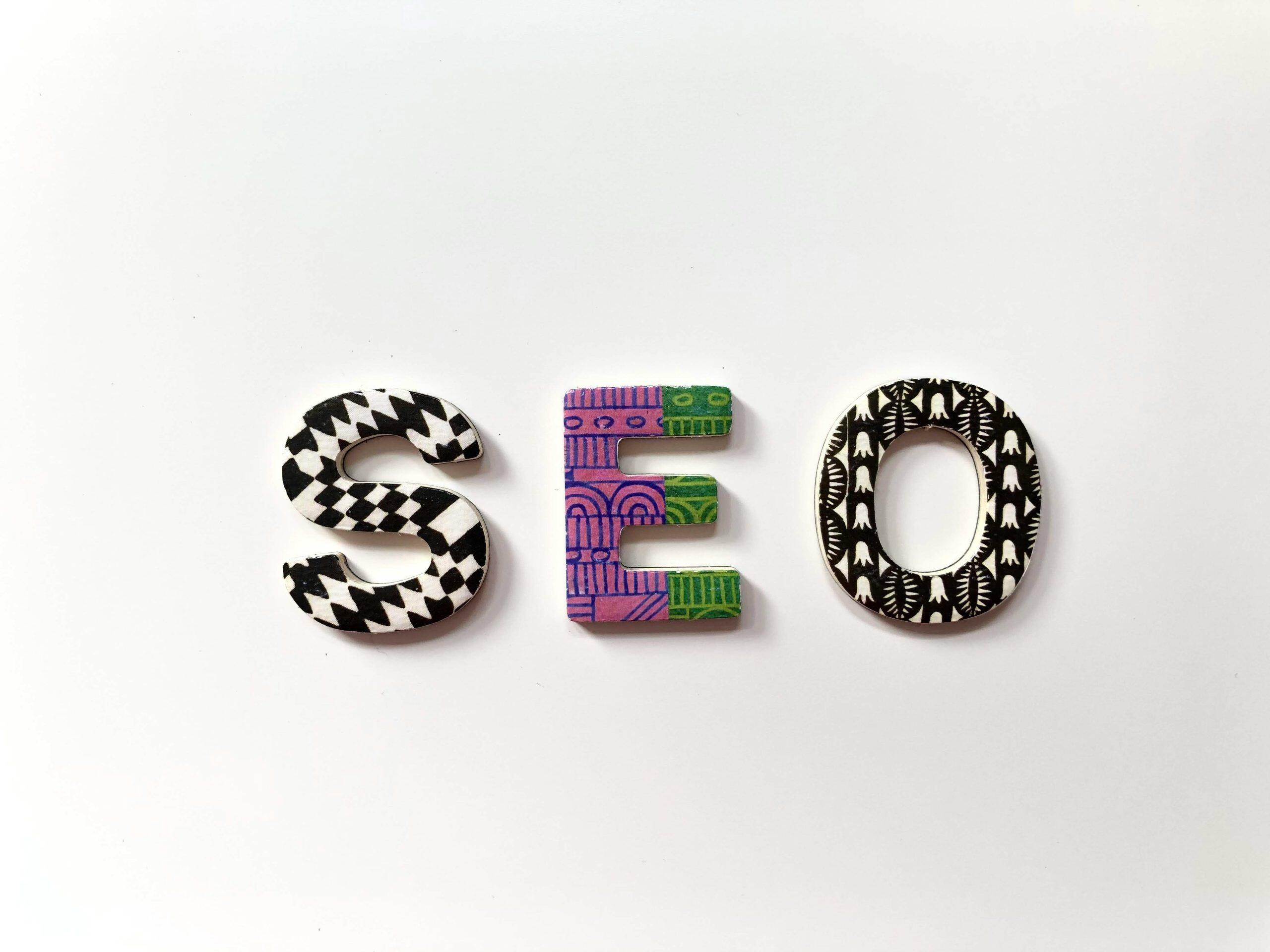 Creative representation of the acronym SEO marketing for small business with three large, stylized letters 'S,' 'E,' and 'O' on a plain white background. Each letter features unique patterns: the 'S' has bold black and white zigzag shapes, the 'E' showcases intricate purple and green geometric designs, and the 'O' displays symmetrical black and white motifs resembling leaves or petals. The letters are evenly spaced, creating a balanced and visually engaging layout.